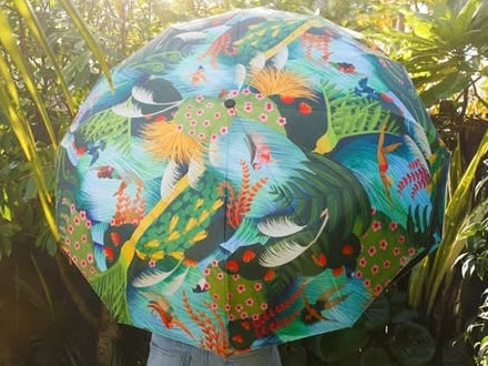 Person holding a colorful umbrella with bird design in a sunlit forest
